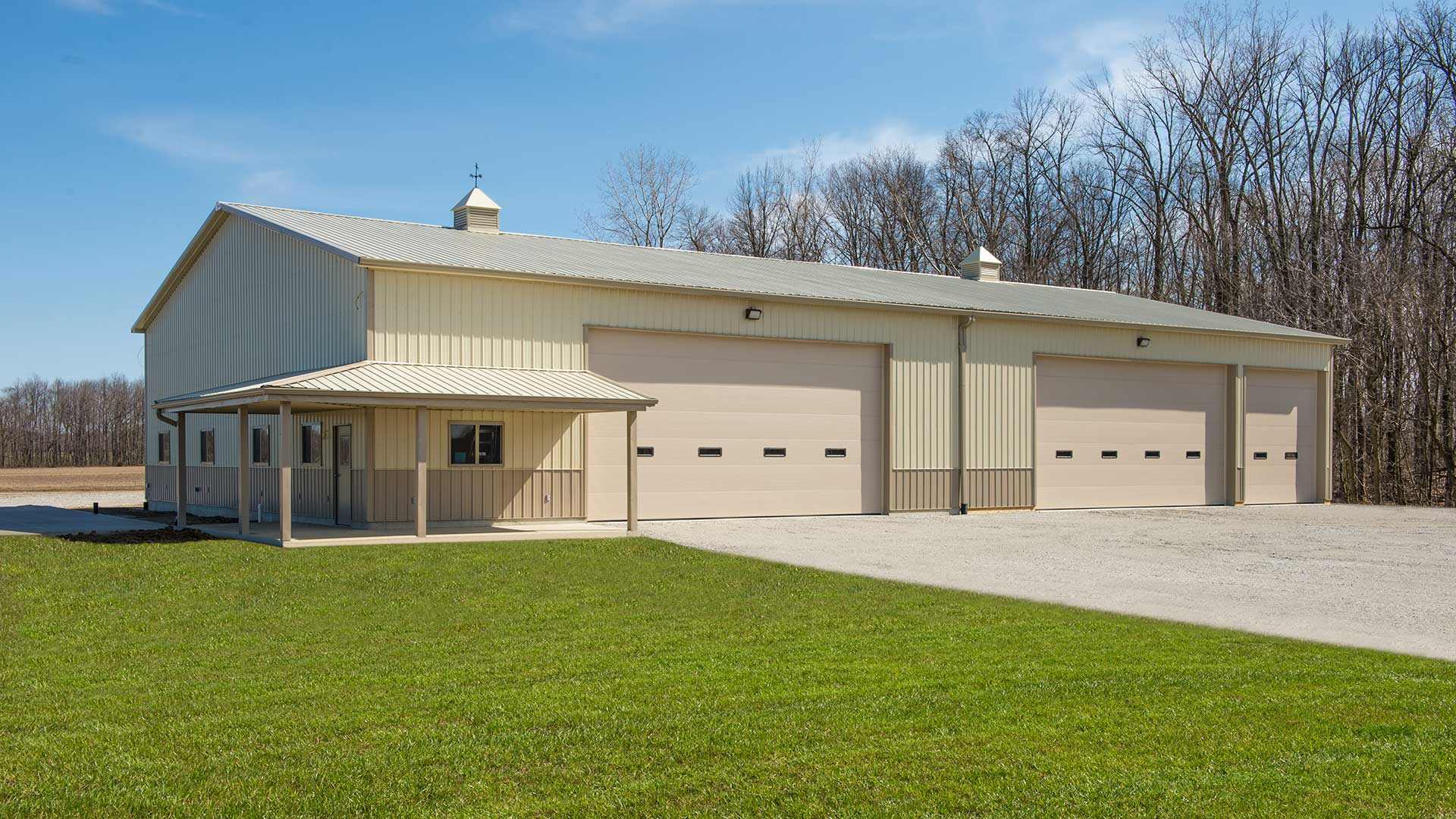 Light-colored metal building with three garage doors beside a grassy property